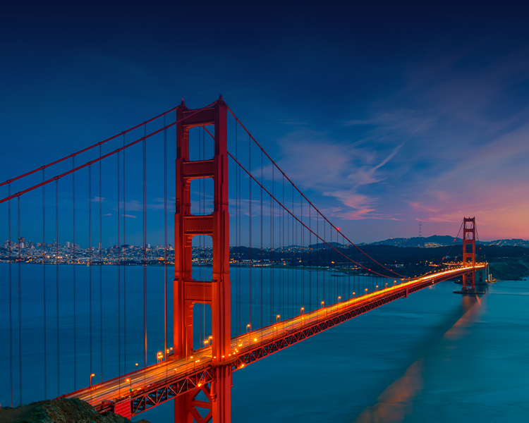 Golden Gate Bridge illuminated at dusk with the San Francisco city skyline in the background.