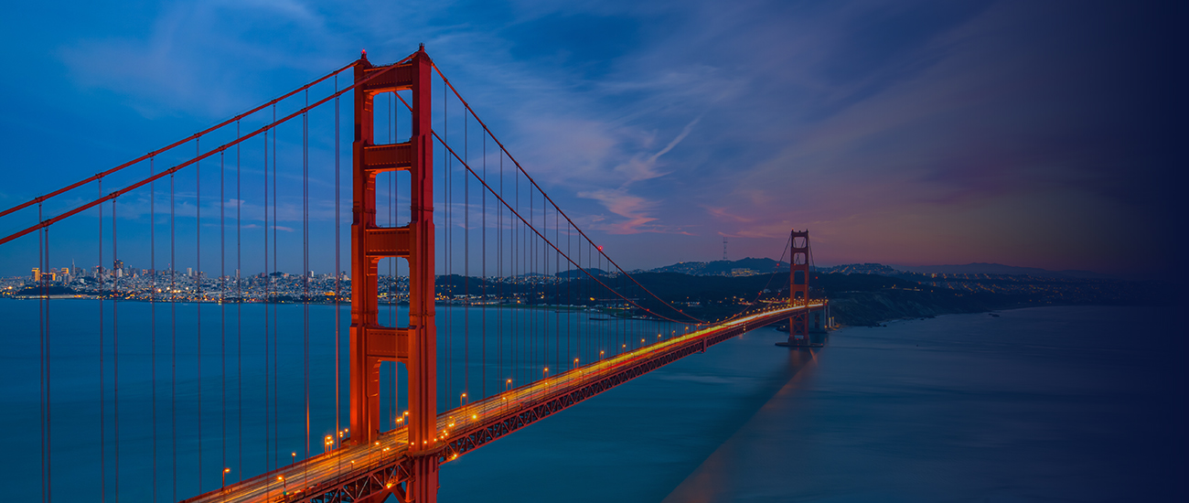 Golden Gate Bridge illuminated at dusk with the San Francisco city skyline in the background.